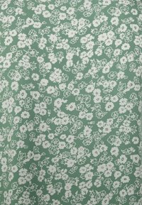 Tissu vert avec un motif floral blanc, présentant de petites fleurs et des feuilles. Le matériau semble doux avec une texture lisse.