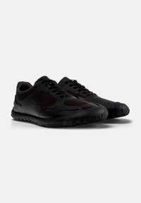 Scarpe atletiche nere con una parte superiore in rete, design elegante, suola texturizzata e sistema di allacciatura. Punta arrotondata e silhouette a profilo basso.