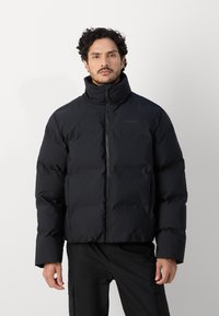 Doudoune noire à col montant, fermeture éclair à l'avant, boudins horizontaux et finition mate, associée à un pantalon cargo noir.