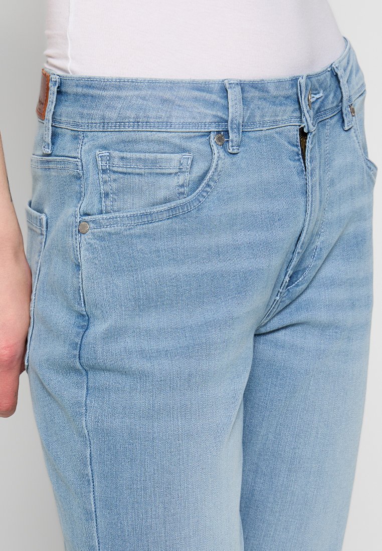 Helle blaue Jeans im Denim-Stil mit klassischem Fünf-Taschen-Design, Reißverschluss und metallischen Akzenten, mit einer leicht ausgewaschenen Textur.