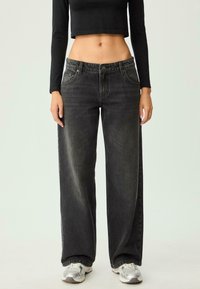 Jeans neri a gamba larga con vita alta, caratterizzati da una texture sbiadita e design a cinque tasche, abbinati a sneakers grigie.