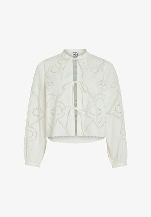 Hvit bluse med lange ermer, dekorert med blomsteraktig hullbroderi, tre knytinger foran, bølget kant og litt puffete ermer med mansjetter og knapper.