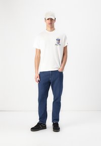 Hvit bomull t-skjorte med et grafisk motiv av en popcornboks, blå denimjeans og svarte joggesko, komplettert med en lyse farget caps.