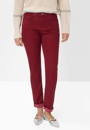 Burgunderfarbene Baumwolljeans mit schlankem Schnitt, Fünf-Taschen-Design und umgeschlagenen Säumen, kombiniert mit silbernen Ballerinas. Weiche Textur und klassischer Knopfverschluss.