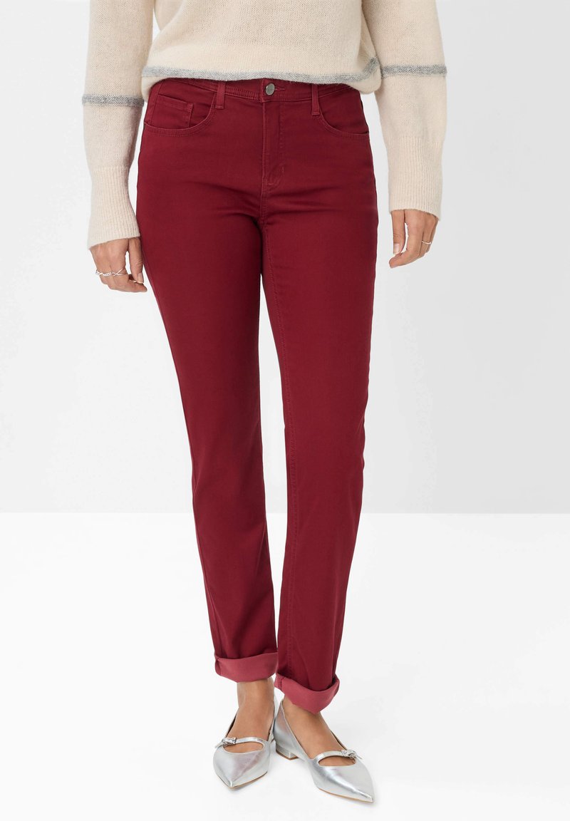 Burgunderfarbene Baumwolljeans mit schlankem Schnitt, Fünf-Taschen-Design und umgeschlagenen Säumen, kombiniert mit silbernen Ballerinas. Weiche Textur und klassischer Knopfverschluss.