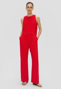 Roter ärmelloser Jumpsuit mit lockerem Schnitt, weitem Bein und minimalen Nähten. Der Stoff wirkt glatt mit einem leicht glänzenden Finish.