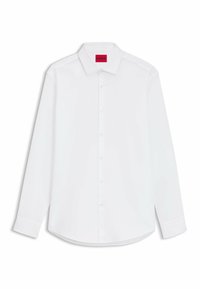 Chemise blanche à manches longues avec col classique. Présente un ourlet arrondi et une étiquette rouge au niveau du col. Tissu en coton doux.