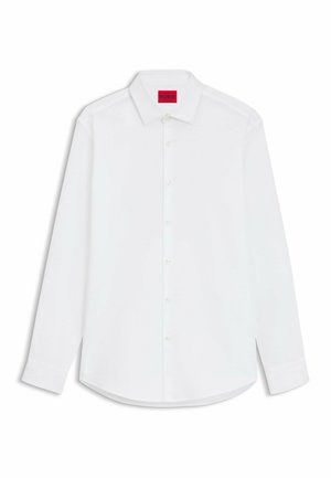 Biała koszula z długim rękawem zapinana na guziki z klasycznym kołnierzykiem. Posiada zaokrąglony dół oraz czerwoną metkę przy dekolcie. Gładki materiał bawełniany.