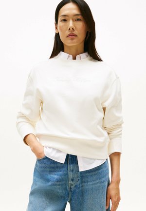 Crème kleurige sweatshirt met een ronde hals, geribbelde mouwen en geborduurd logo. Draag een witte blouse eronder en blauwe jeans.