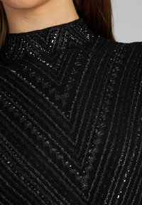 Schwarzes, strukturiertes Kleid mit hohem Kragen und einem Zickzackmuster, verziert mit metallischen Pailletten und Perlen, die einen schimmernden Effekt erzeugen.