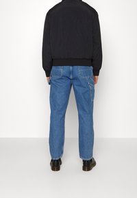 Černá bomber bunda s žebrovaným spodním lemem a rukávy, která je kombinována se světle modrými džíny rovného střihu s kapsami na zadní straně. Černé boty dotvářejí celkový vzhled.