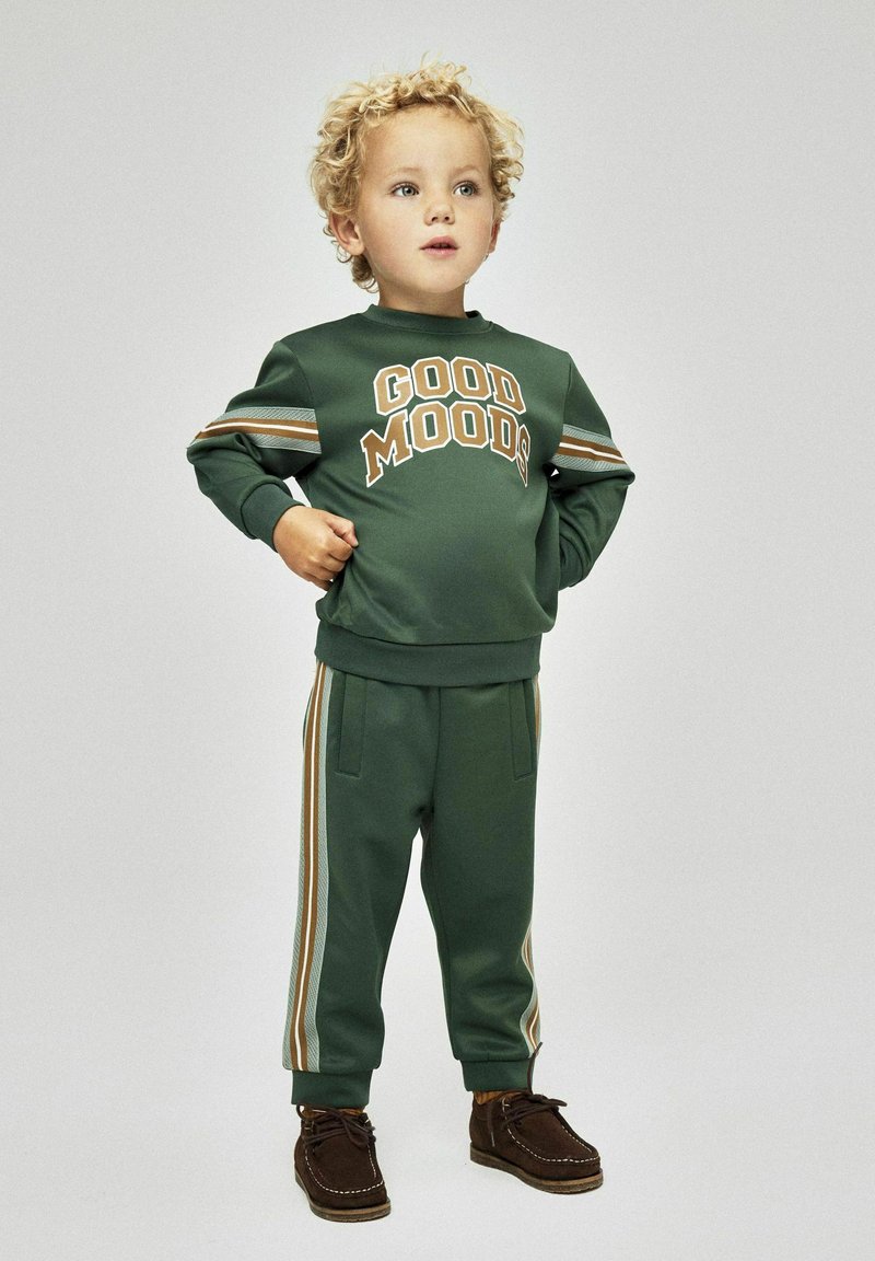 Sweatshirt vert avec "GOOD MOODS" en beige, associé à un pantalon de jogging assorti avec des rayures sur les côtés en beige, crème et rouille ; tissu doux.