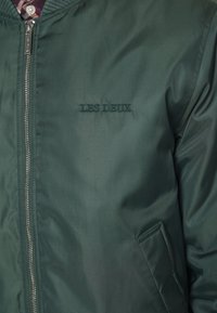 Veste zippée verte avec "LES DEUX" brodé sur la poitrine gauche et une poche passepoilée côté droit.