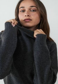 Dunkelgrauer, übergroßer Rollkragenpullover mit gerippten Bündchen und einer weichen, flauschigen Textur. Der Kragen ist an der Vorderseite leicht umgeschlagen.