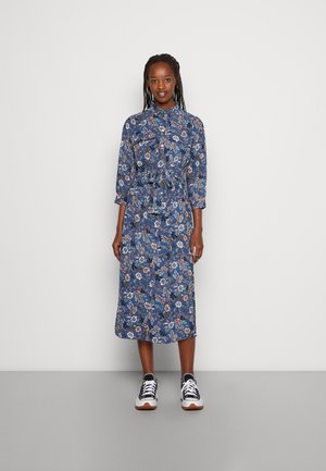 Floral midi dress in blue with three-quarter sleeves, tie waist, front buttons, featuring a diverse pattern of flowers and foliage. Paired with black and white sneakers.