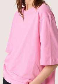 Camiseta de algodón rosa con ajuste relajado, mangas cortas y escote redondo. La tela parece suave con costuras mínimas.