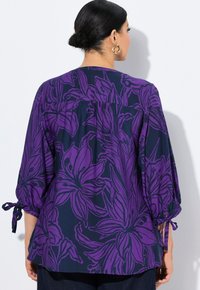 Lilla bluse med blomstermønster på en marineblå baggrund, med lette ærmer og snore ved manchetterne. Blødt materiale med en afslappet pasform.