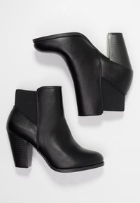 Sorte læder ankelstøvler med stablede blokhæle og elastiske sidepaneler, vist på en lys baggrund set oppefra.