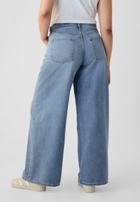 Lichtblauwe wijde broekspijpjans met een hoge taille, voorzien van twee achterzakken en een subtiele textuur. Gecombineerd met beige sneakers.