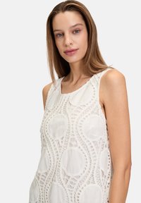 Weißes ärmelloses Kleid mit aufwändigen Spitzenverzierungen in kreisförmigen Mustern, strukturiertem Stoff und Rundhalsausschnitt.