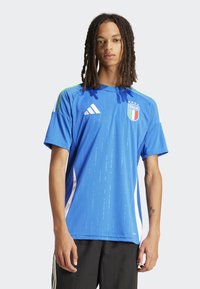 Maillot de sport bleu arborant le drapeau italien, trois étoiles blanches, des accents verts et des rayures texturées sur un tissu lisse. Panneaux latéraux blancs.