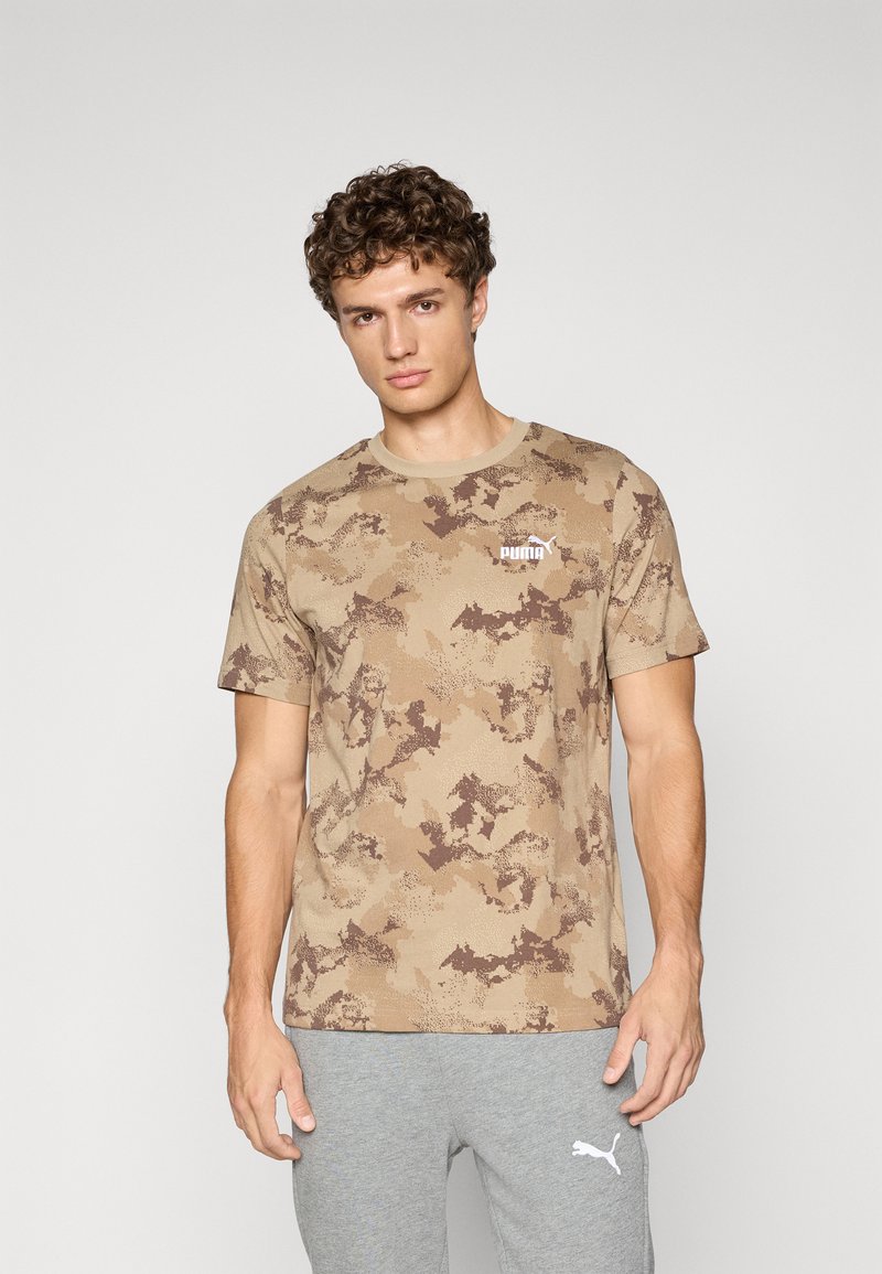 T-shirt en coton avec un motif camouflage dans des tons de beige et de marron, présentant un col rond et un petit logo blanc sur la poitrine.