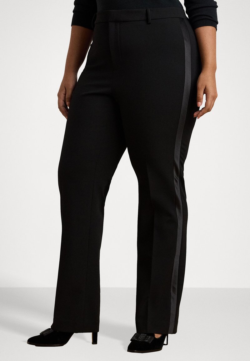 Čierne nohavice strihané na mieru s rovnými nohavicami, s lesklým bočným pruhom a hladkou textúrou. Skombinované s čiernymi lodičkami na podpätku.