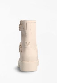 Botín de tobillo de imitación de cuero beige con punta redondeada, doble hebilla lateral, detalle del logo en el talón y suela de goma blanca gruesa.