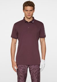 Mörkröd polotröja med tre knappar, kortärmad och en logotyp på kragen. Matchas med mönstrade mörkröda byxor.