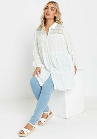 Camicia bianca con bottoni e dettagli in pizzo, maniche voluminose, abbinata a jeans skinny blu chiaro e sandali espadrillas bianchi con cinturino.