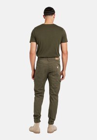 T-shirt in cotone verde oliva e pantaloni cargo abbinati con polsini elastici e tasche utili, visti da dietro. Texture morbida, design semplice.