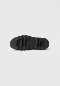 Black rubber shoe sole featuring textured patterns, grooves for traction, and a solid, rounded shape. Smooth finish with a flat outline.