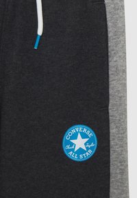 Grå och svarta joggers med en mjuk textur, som har en blå Converse All Star-logotyp och vita snörningsdetaljer.
