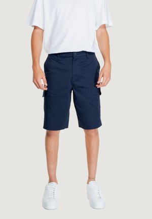 Pantalones cortos tipo cargo azul marino de mezcla de algodón, con bolsillos laterales, cierre de botón y un corte relajado, combinados con zapatillas blancas.