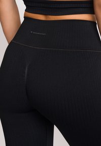 Zwarte geribde legging met hoge tailleband, voorzien van een subtiele logo op de achterkant, gladde textuur en naaddetails bij de taille en benen.