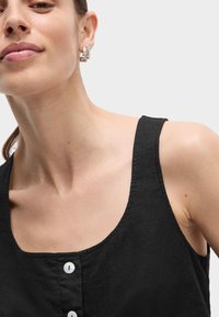 Zwarte linnen tanktop met een ronde hals en drie witte knopen. Heeft een gestructureerde stof en brede schouderbanden.