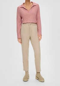 Långärmad, rosa tröja med krage; matchad med beige byxor med elastisk midja och beige ankelstövlar med tjocka sulor.