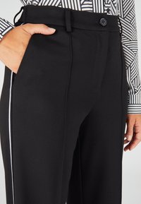 Zwarte broek met een gladde textuur, voorzien van zijzakken, een knoopsluiting en witte bies langs de buitenste naden.