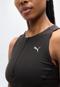 Μαύρο αθλητικό τοπ με κλείσιμο με φερμουάρ και στρογγυλεμένο ντεκολτέ, με μικρό λευκό λογότυπο Puma στην αριστερή πλευρά. Λεπτή υφή.
