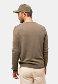 Khaki tröja med ribbat mönster och rundad hals, parat med en kordflöjlsmössa. Bakgrunden är neutral, vilket framhäver plaggen.