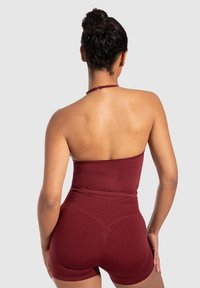 Bordeauxkleurig, rekbaar body met halternek, naadloos ontwerp en hoge taille shorts. Effen textuur met een getailleerd silhouet.