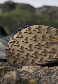 Shoe sole with rugged tread pattern on rocky ground, featuring Continental branding for outdoor or hiking footwear.