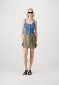 Cropped denim top with button detailing, paired with a green wrap skirt and black open-toe slides, set against a plain background.