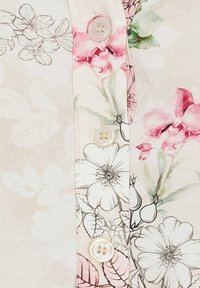 Blomsterstof med blød beige baggrund, prydet med pink og hvide blomster, og fire runde plastknapper langs fronten.