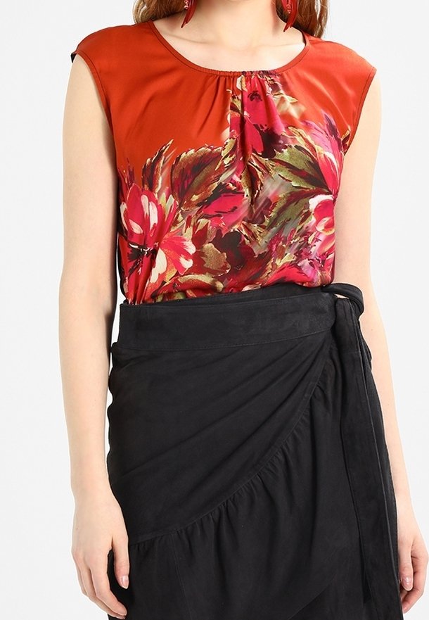 Kvinna som bär en ärmlös röd blommig blus instoppad i en hög midje svart omslagskjol med en sidoknut.