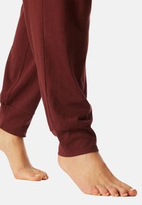 Bordeauxkleurige sweatpants met een zachte textuur, taps toelopende enkels en zijzakken, gedragen met blote voeten.