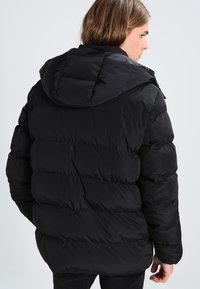 Sort pufferjakke med hætte, med en kviltet design, vandrette sektioner og en glat, blank overflade.