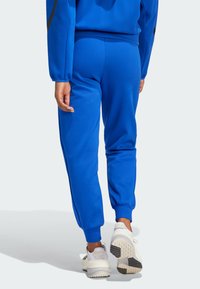 Person wearing blue jogger pants and white sneakers, shown walking away against a plain light background.