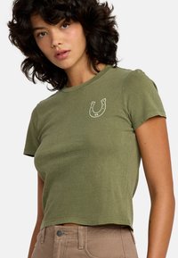 Oliwkowa, krótkozdbna crop top z miękkiej bawełny, z białą grafiką w kształcie podkowy z napisem "VA" na klatce piersiowej. Prosty, dopasowany krój.