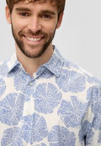 Lichte button-up shirt met een witte achtergrond en gedurfde blauwe bladdessins. Voorzien van een klassieke kraag en subtiele textuur.